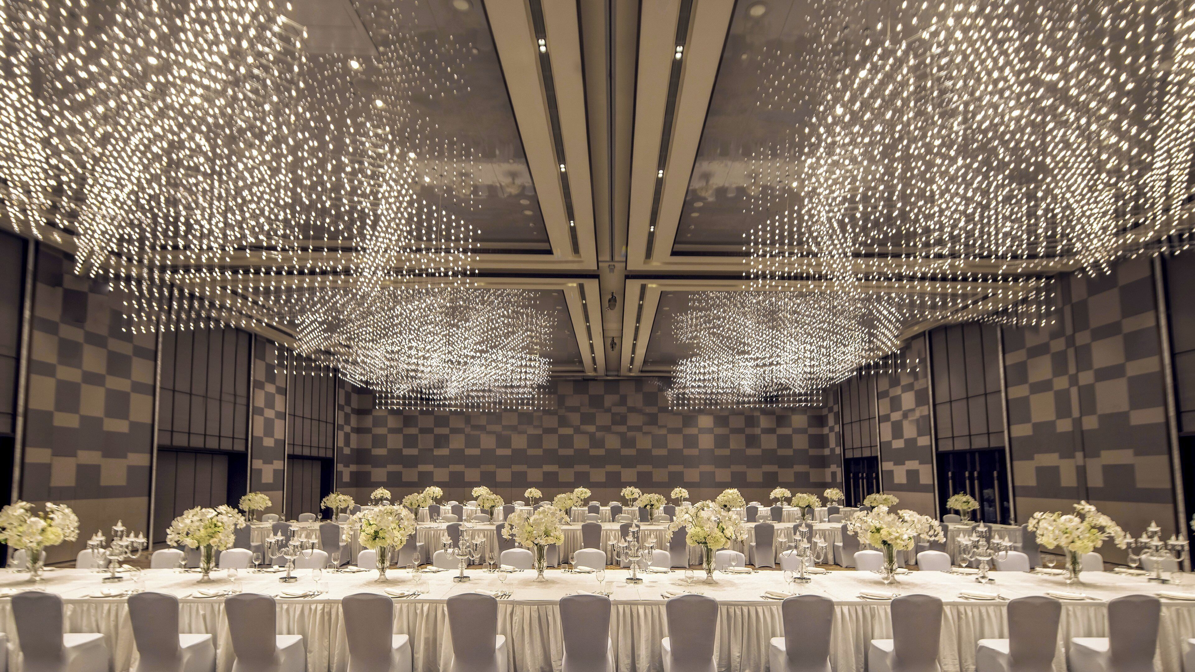 A banquet hall with tables set for a formal event, featuring a checkered wall pattern and a ceiling with a unique light fixture design.