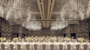 Un salón de banquetes con mesas dispuestas para un evento formal, destacando un diseño de pared con patrón de cuadros y un techo con una lámpara de diseño único.