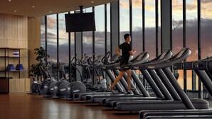 A gym with multiple treadmills, a large window with a view of the sky, and a television screen. - InterContinental Tianjin Yujiapu Hotel & Residences by IHG (Tianjin)