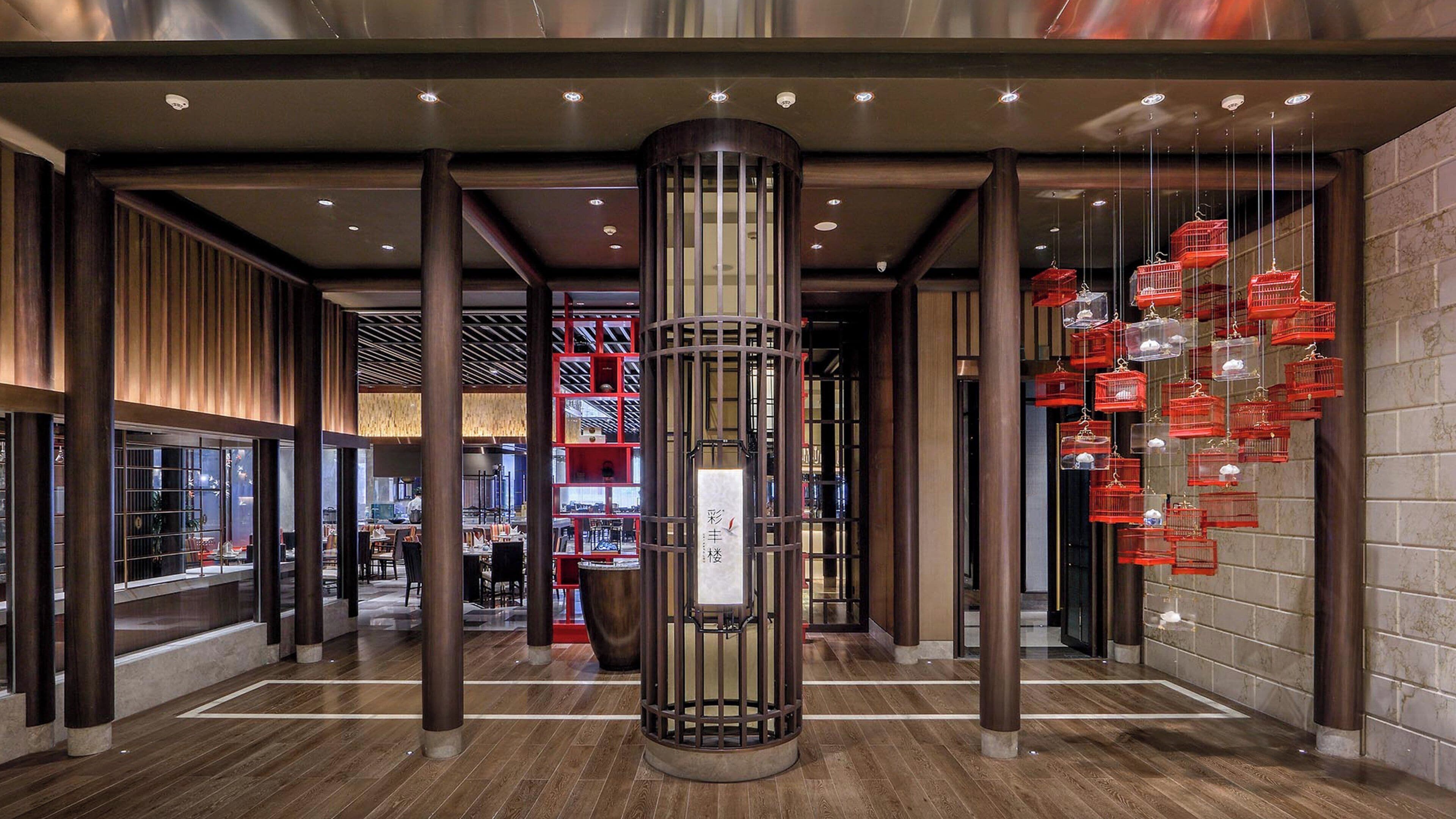 A modern interior with a central column, wooden flooring, and red birdcage decorations.
