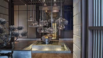 A modern interior with a central water feature, multiple hanging light fixtures, and a wooden floor.
