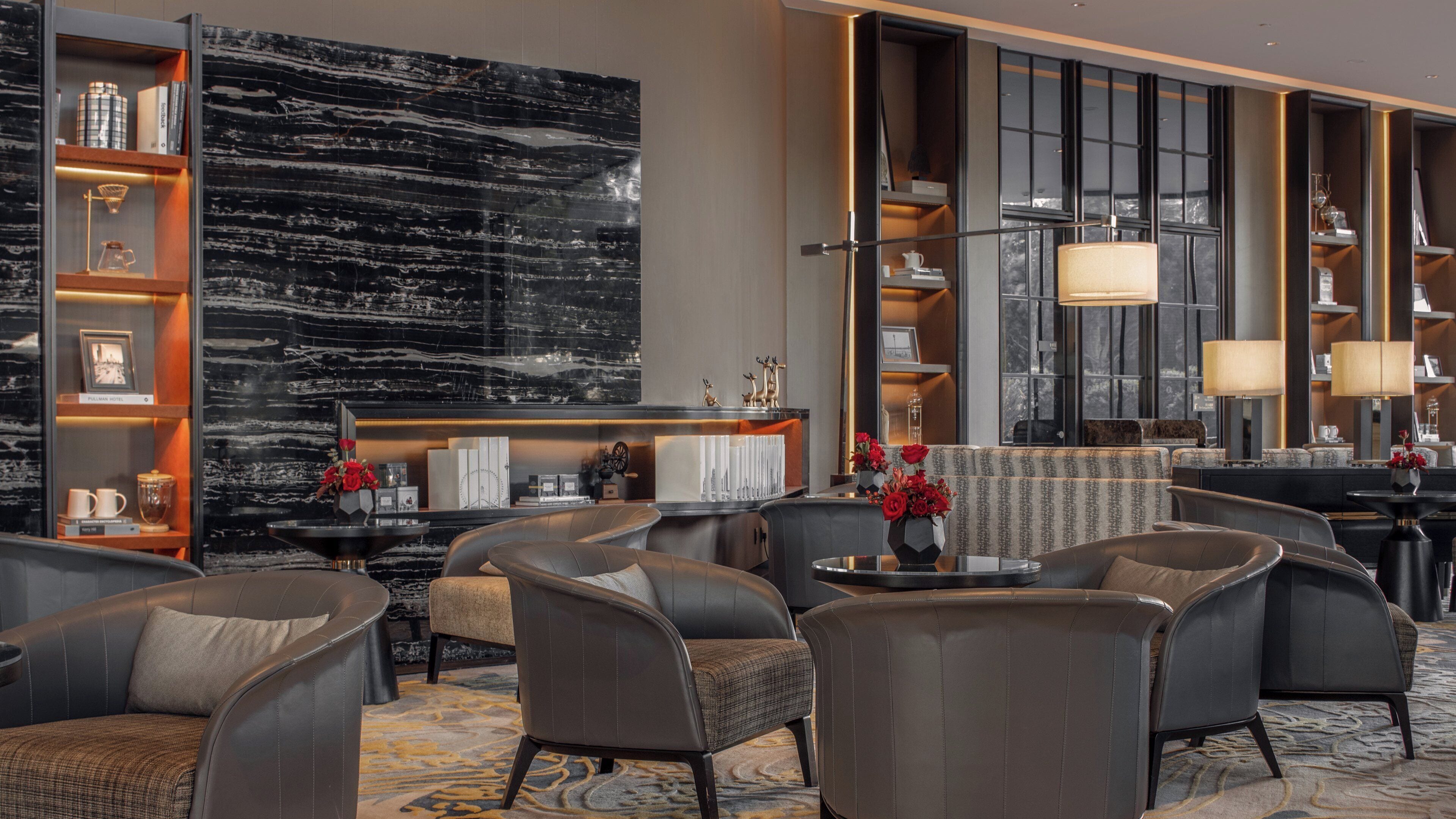 A modern hotel lobby with leather seating, a marble wall, and a large window.