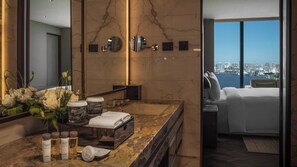 Un baño moderno con encimera de mármol, un espejo grande y vistas a un paisaje urbano a través de un ventanal.