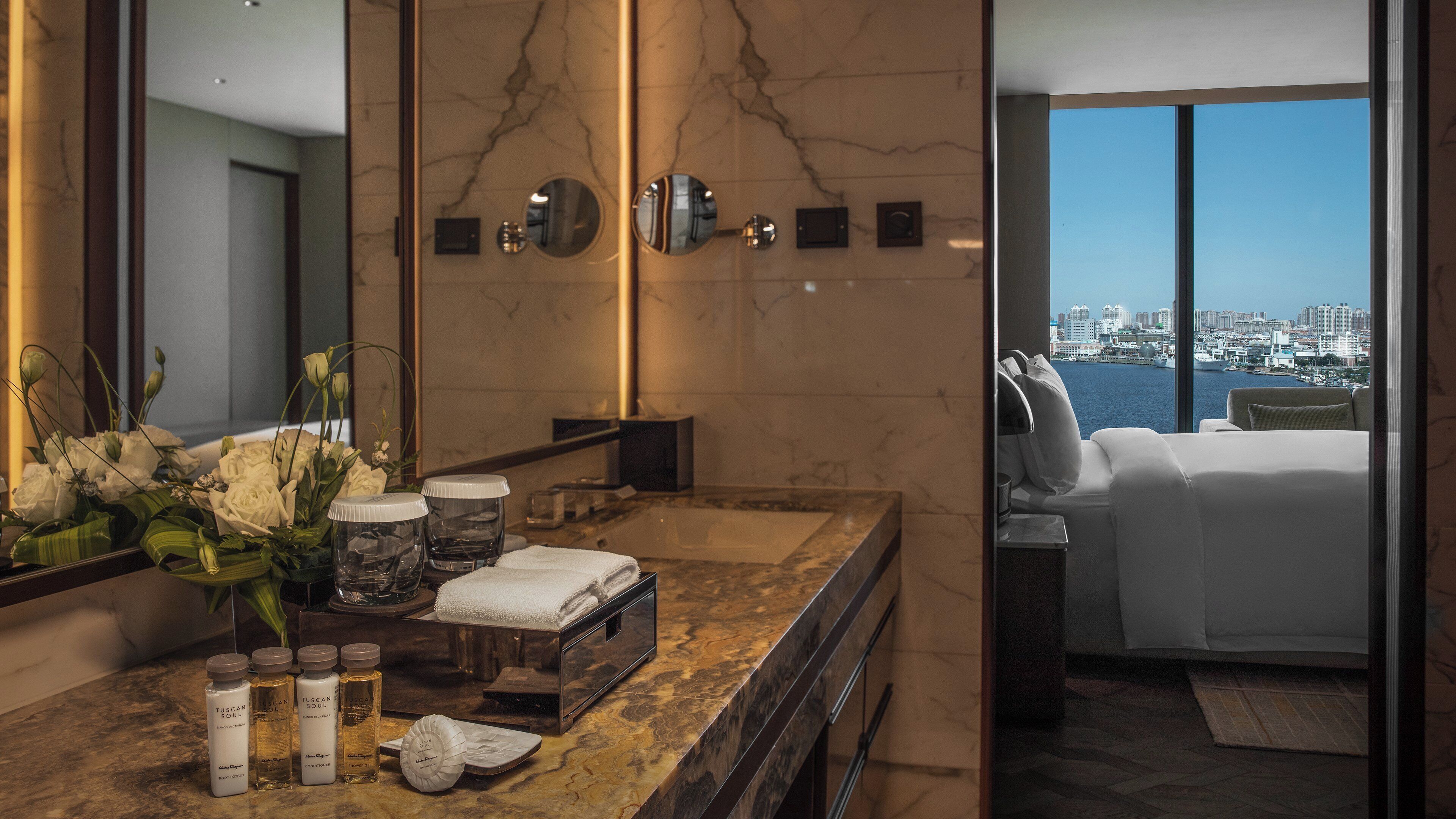 A modern bathroom with a marble countertop, a large mirror, and a view of a cityscape through a large window.