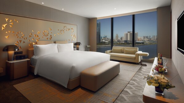 Una habitación de hotel moderna con una cama grande, un sofá, un escritorio con un florero y vistas a un horizonte urbano.