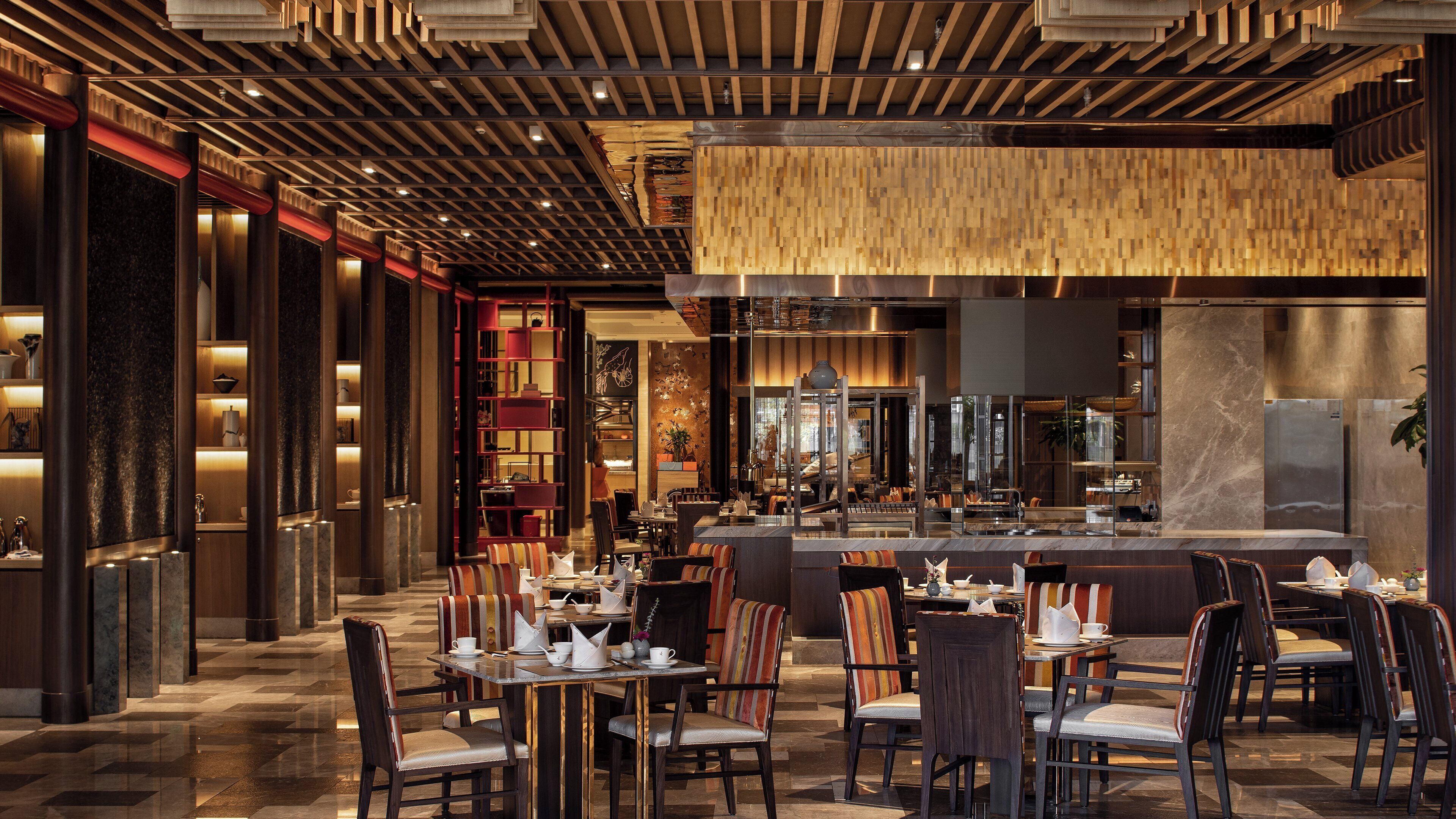 A modern restaurant with a bar area, seating arrangements, and a decorative ceiling.