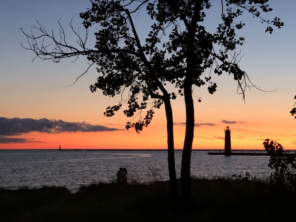 A sunset over a body of water with a lighthouse in the distance. - Charming RedBird Cottage- On A Back Dune, Walk To The Beach (Muskegon)
