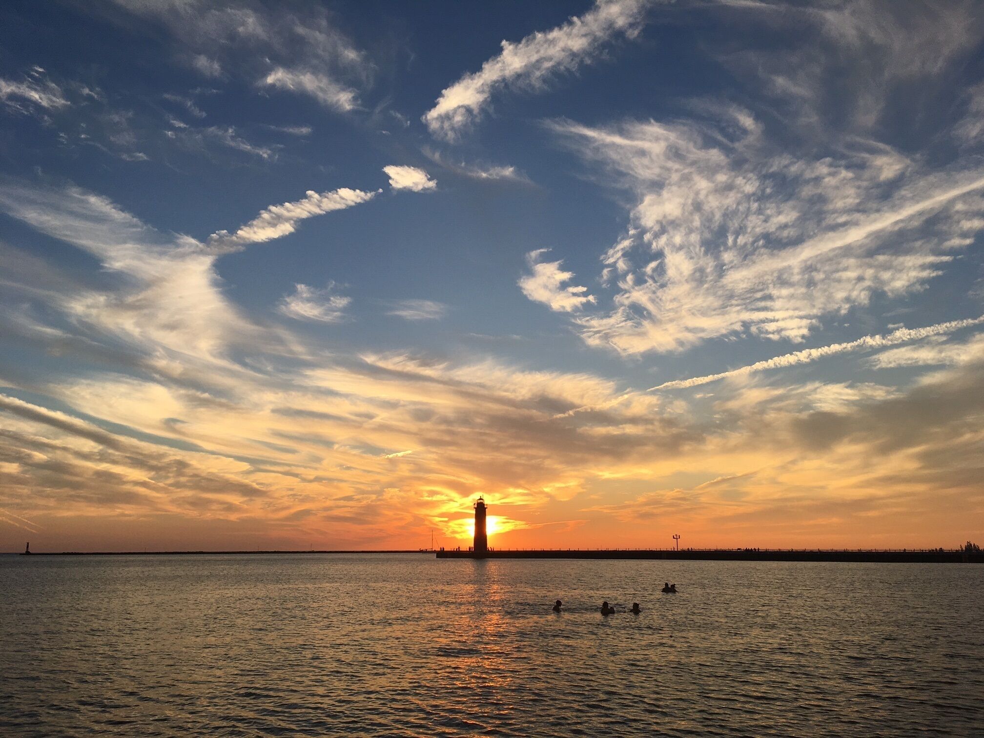 A sunset over a calm body of water with a lighthouse in the distance.