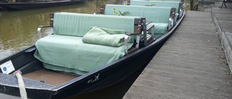 A row of green-covered boat beds on a narrow waterway, with a wooden dock and a bridge in the background.