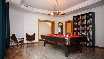 A pool table with balls, two folding chairs, a bookshelf, and a clock on the wall.