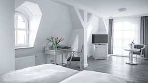 Quarto de hotel moderno com cama, escrivaninha, cadeira, televisão e um pequeno espaço de refeições.