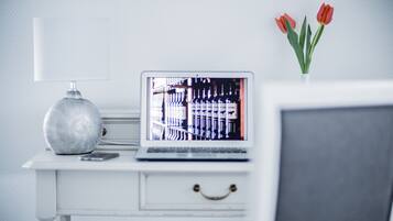 Un ordinateur portable sur un bureau blanc, avec un vase de tulipes et une lampe.