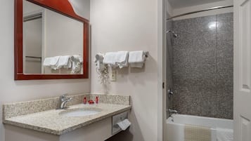 Casa de banho com lavatório de bancada em granito, espelho, secador de cabelo e área de duche.