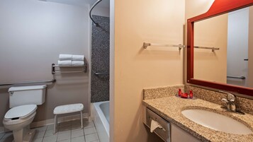 Un baño con inodoro, ducha, lavamanos con encimera de granito y espejo.