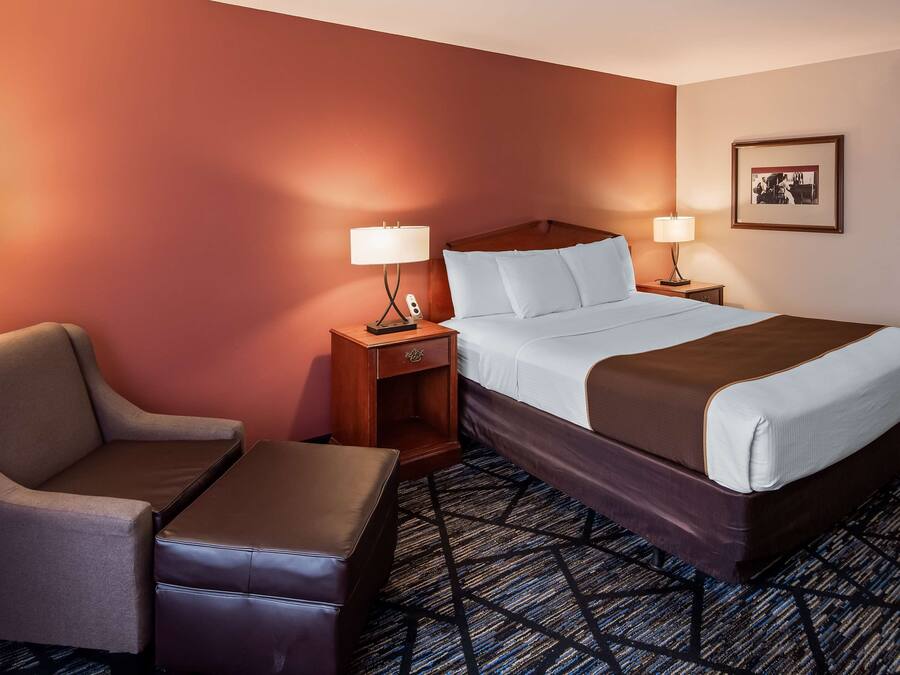 Quarto de hotel com uma cama, duas mesas de cabeceira com abajures, uma cadeira e uma pequena mesa.