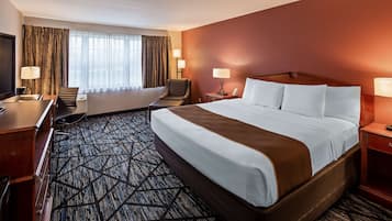 A hotel room with a large bed, a desk, a chair, a television, and two lamps.