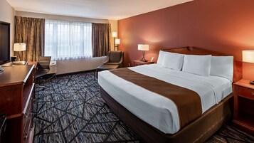 Una habitación de hotel con una cama grande, un escritorio, una silla, un televisor y dos lámparas.