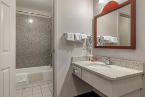 A bathroom with a granite shower wall, a white sink with a granite countertop, and a mirror with a wooden frame.