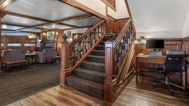 Une pièce spacieuse avec un escalier en bois, un bureau avec un ordinateur et des sièges confortables.