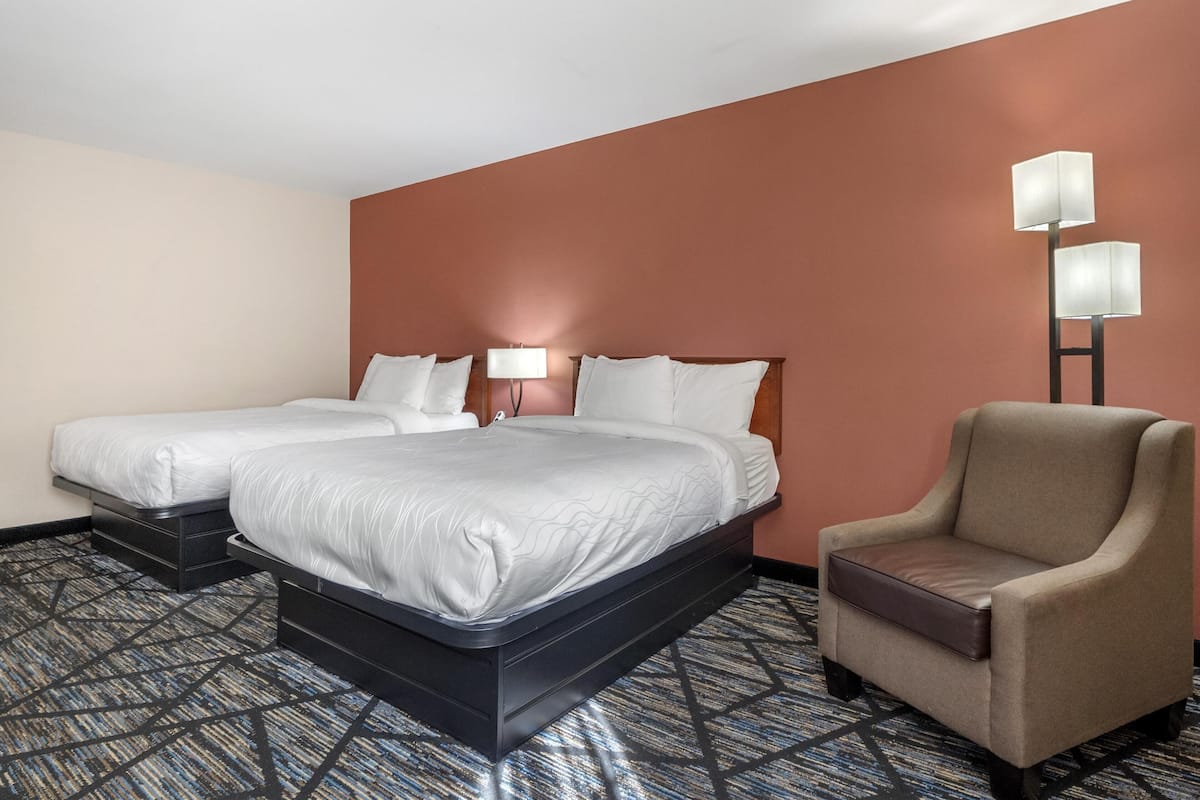 A hotel room with two beds, a chair, and a lamp.