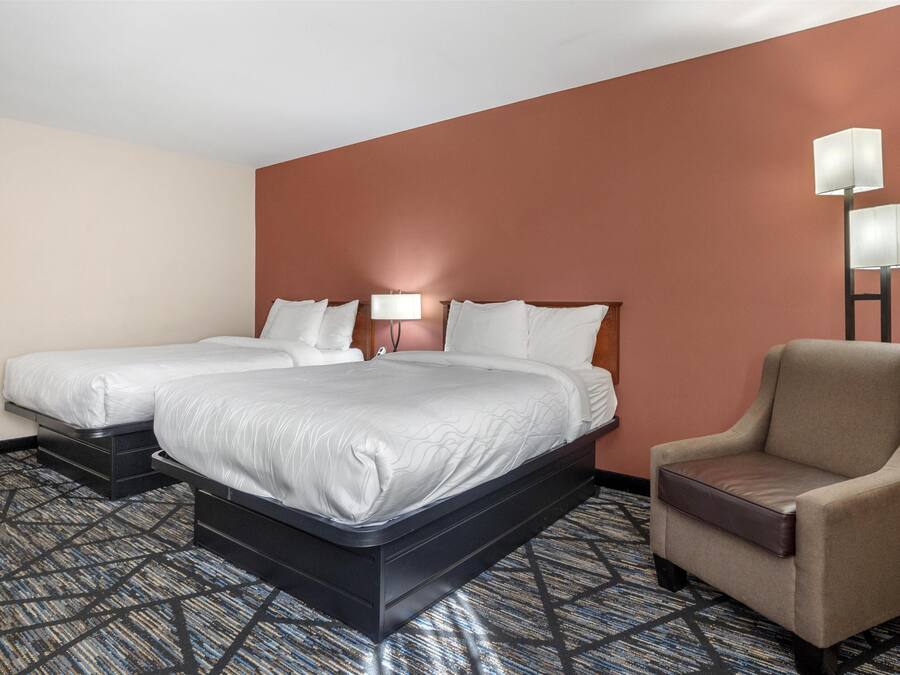 Habitación de hotel con dos camas, una silla y una lámpara.