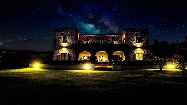 A stone building with a central archway and two wings, illuminated by ground lights, under a starry night sky. - Borgo Antico XIX sec (Gesturi)