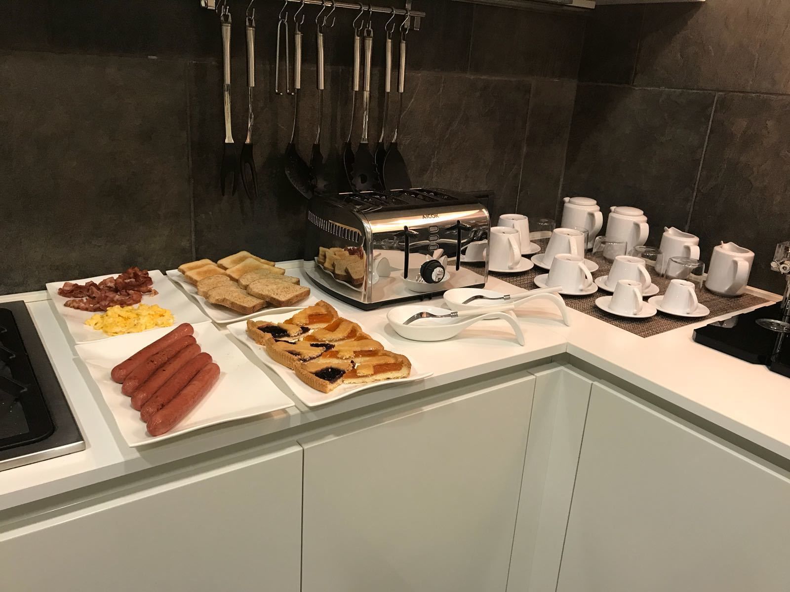 Un bufé de desayuno con hot dogs, huevos revueltos, tostadas y una tarta.