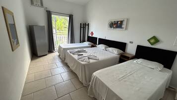 A hotel room with two single beds, a small table, a chair, a TV, and a window with curtains.