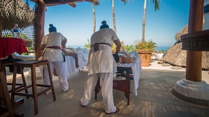 Un salon de massage offrant une vue sur l’océan, doté de meubles en bois et de toits de chaume.