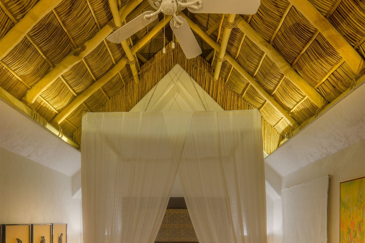 Una habitación con una cama bajo un dosel, un ventilador de techo y obras de arte enmarcadas en las paredes.