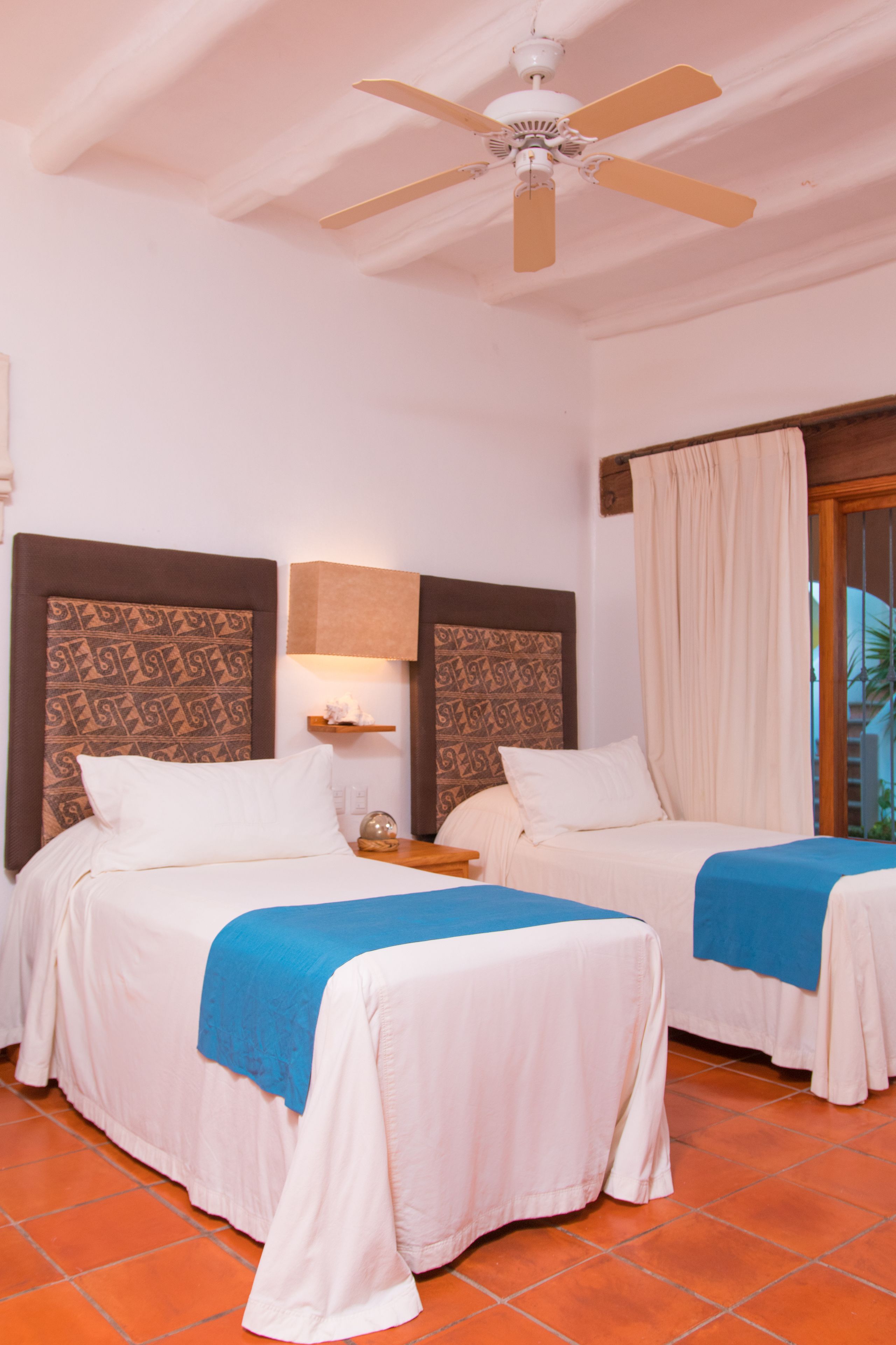 A hotel room with two beds, a ceiling fan, a nightstand, and a window with curtains.
