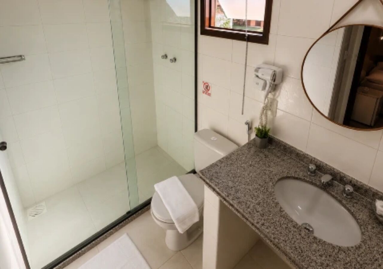 Un baño con cabina de ducha de vidrio, inodoro, lavamanos y espejo.