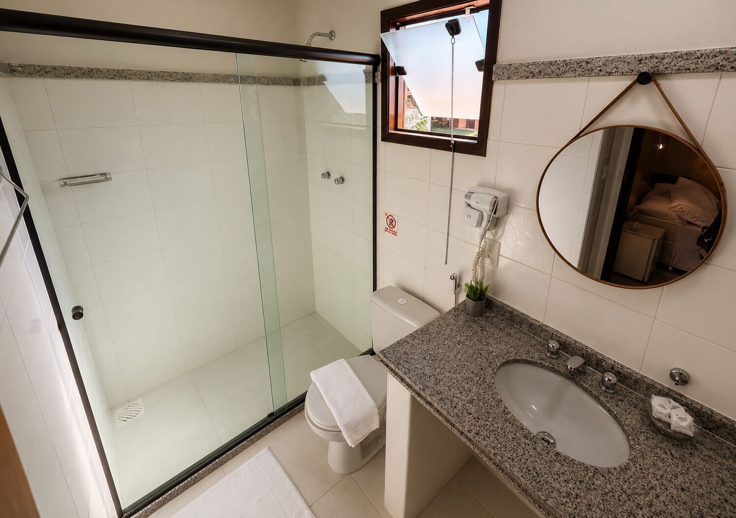 A bathroom with a glass shower enclosure, a toilet, a sink with a granite countertop, and a mirror.