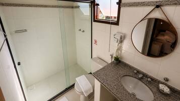 Um banheiro com box de vidro, vaso sanitário, pia com bancada de granito e espelho.