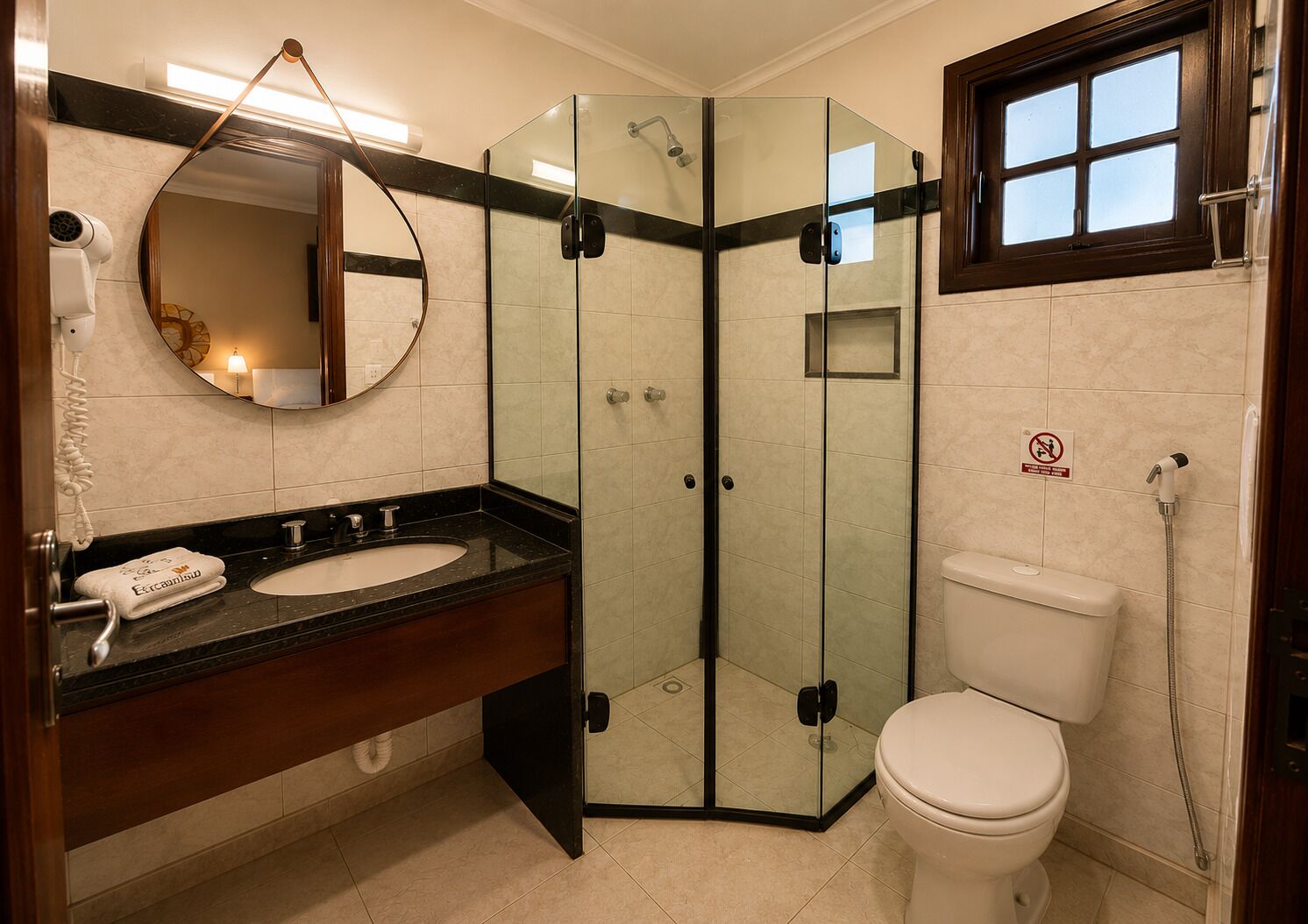 Uma casa de banho com cabine de duche em vidro, sanita branca, lavatório com espelho e porta-toalhas com toalha.