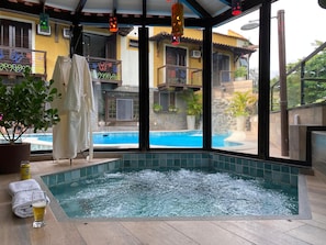 A spa area with a hot tub, towels, and a glass of beer. - Hotel Casa Encantada Penedo (Itatiaia)