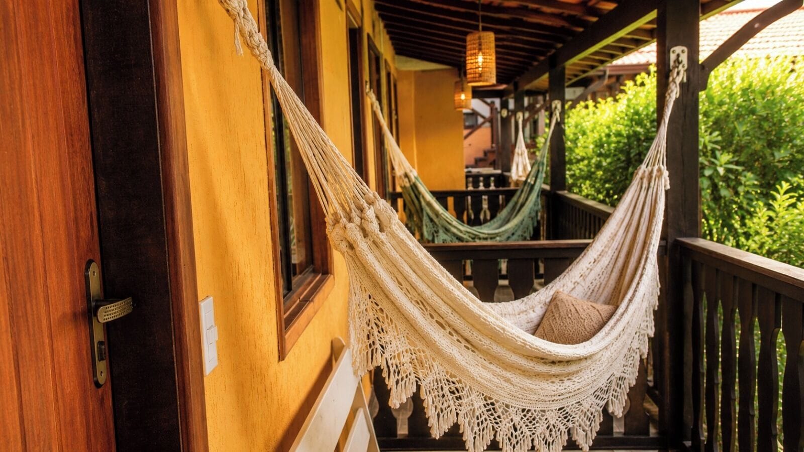 A hammock on a porch with a wooden railing and a door.