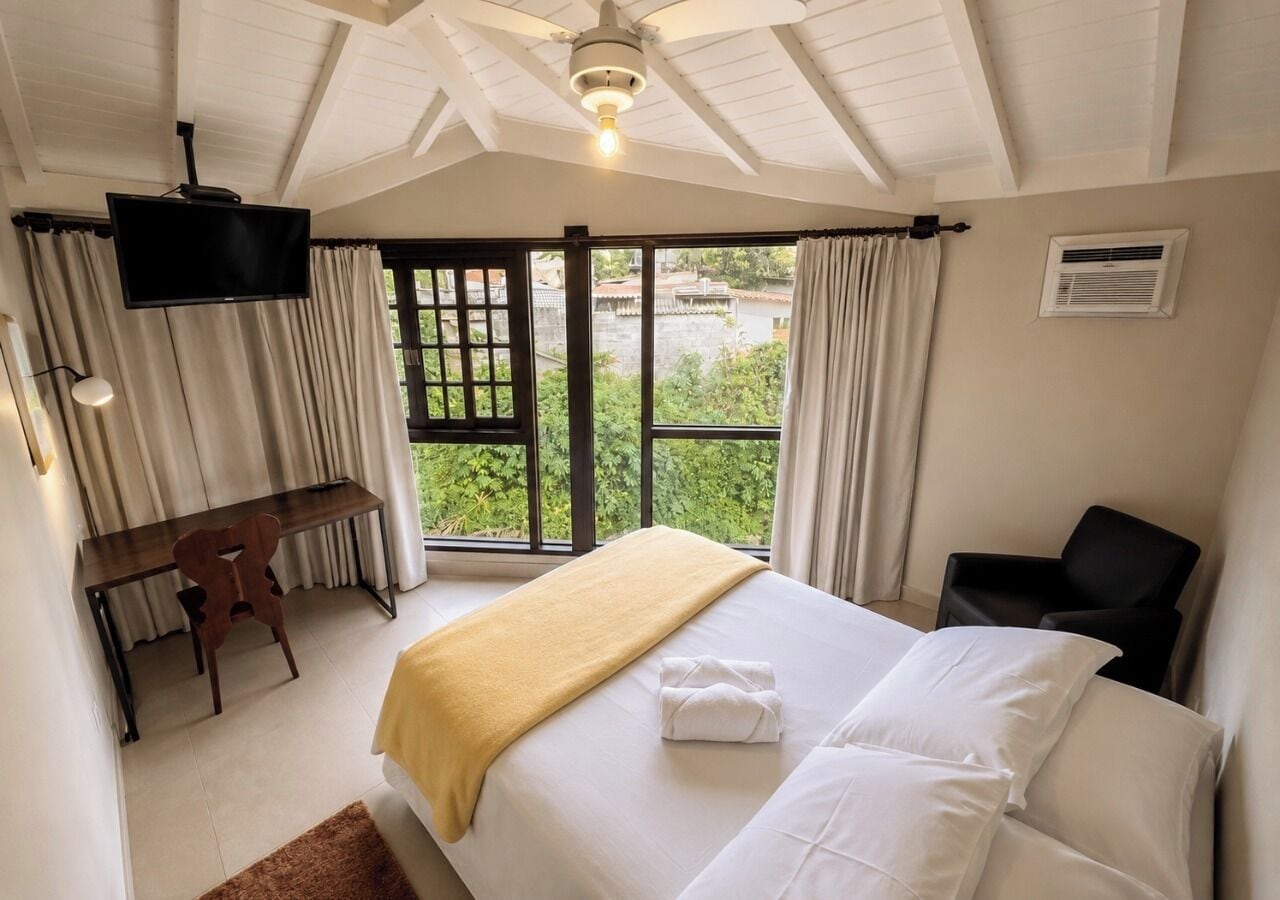 Habitación de hotel con cama, escritorio, silla, televisor y vista a espacios verdes.