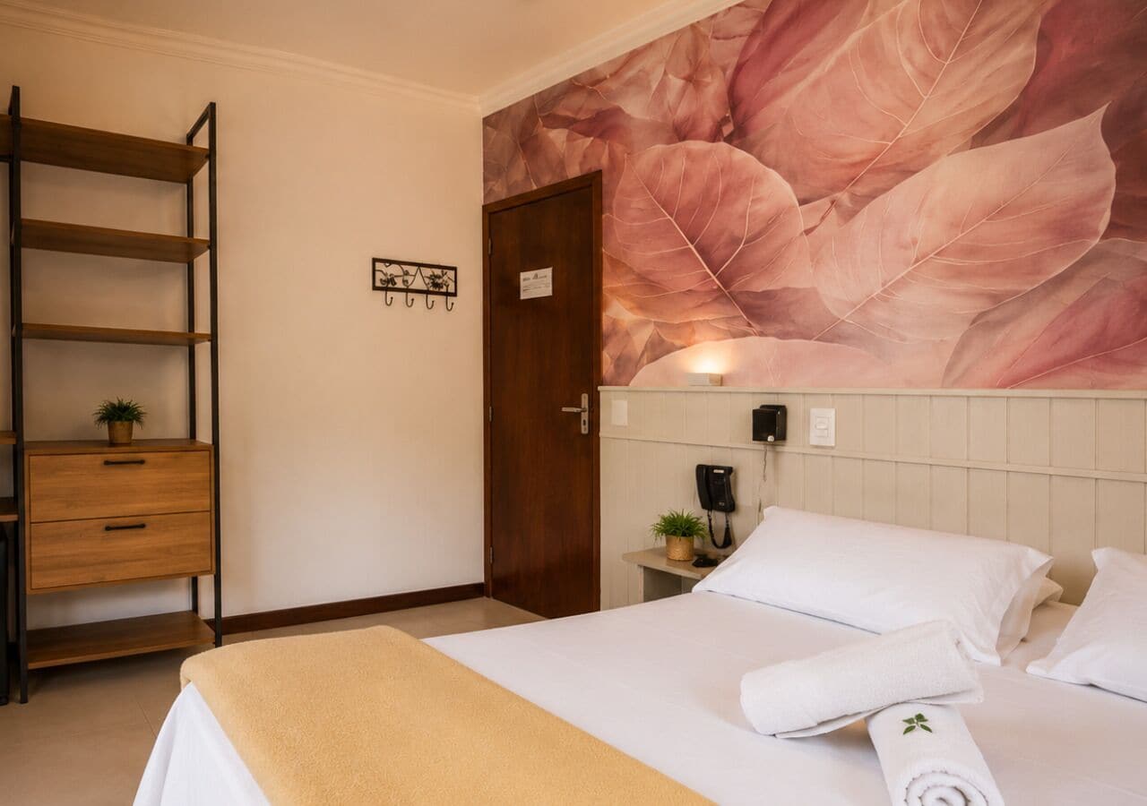 A hotel room with a bed, a wooden shelf, a wall-mounted phone, and a door.