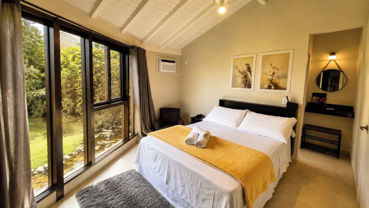 A bedroom with a large bed, a bedside table, a chair, and a window with curtains.
