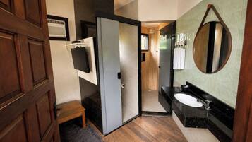 Un baño moderno con puerta de madera, un pequeño banco, un espejo, un lavamanos y una zona de ducha.
