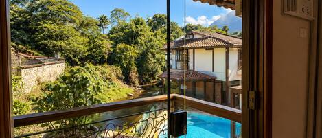 A balcony with a view of a swimming pool, lush greenery, and a mountain in the background.