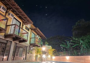 A two-story building with balconies, a stone wall, and a waterfall feature. - Hotel Casa Encantada Penedo (Itatiaia)