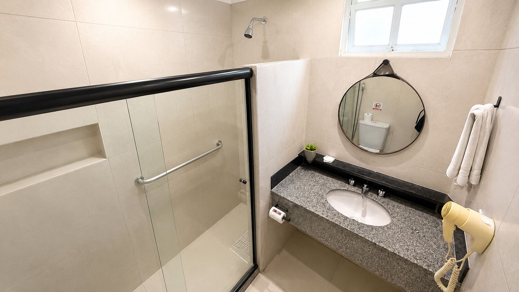 Uma casa de banho com cabine de chuveiro em vidro, lavatório com porta-toalhas e espelho.