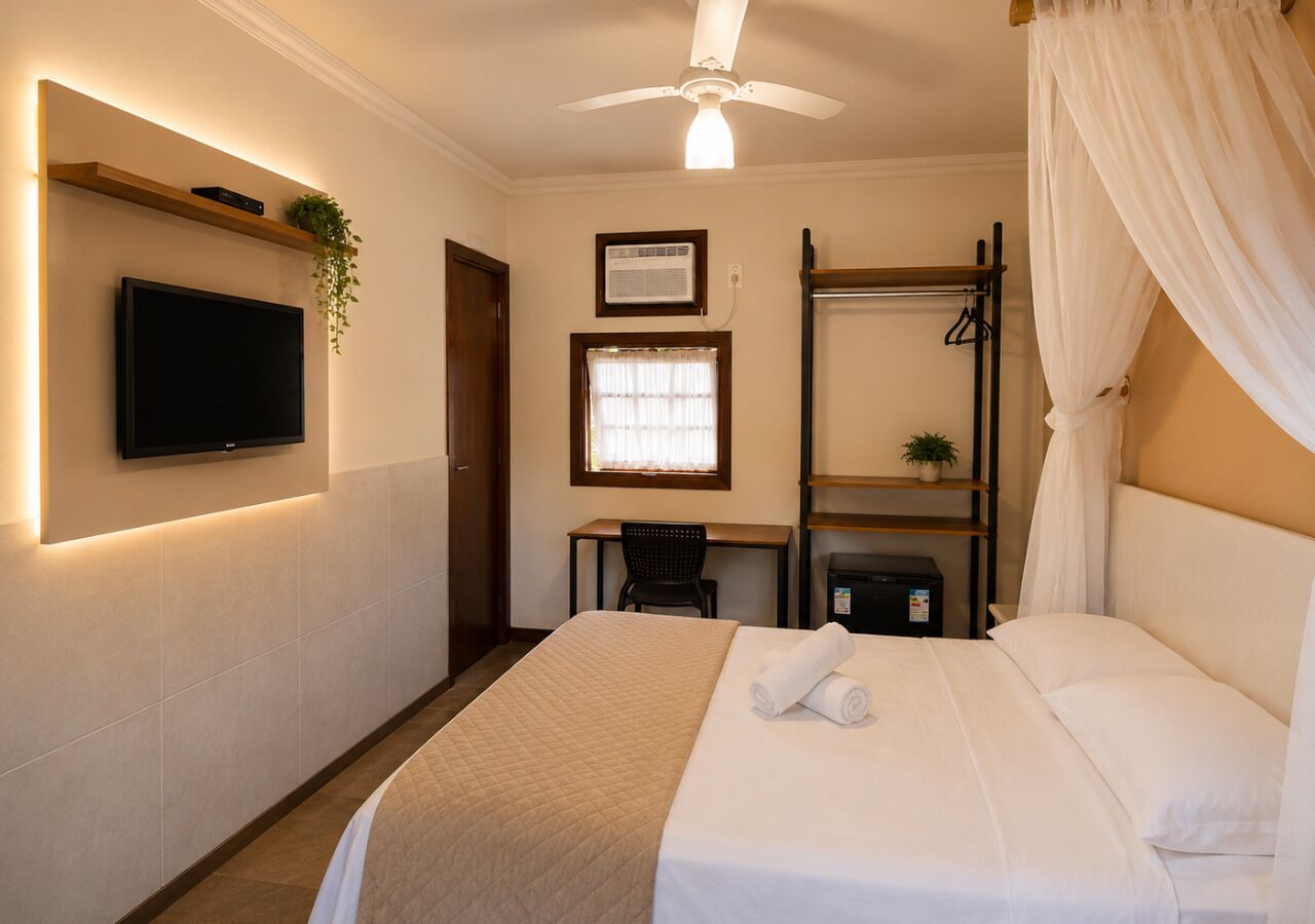 Quarto de hotel com cama, escrivaninha, cadeira, televisão e ventoinha no teto.