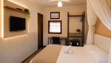 Quarto de hotel com cama, escrivaninha, cadeira, televisão e ventoinha no teto.