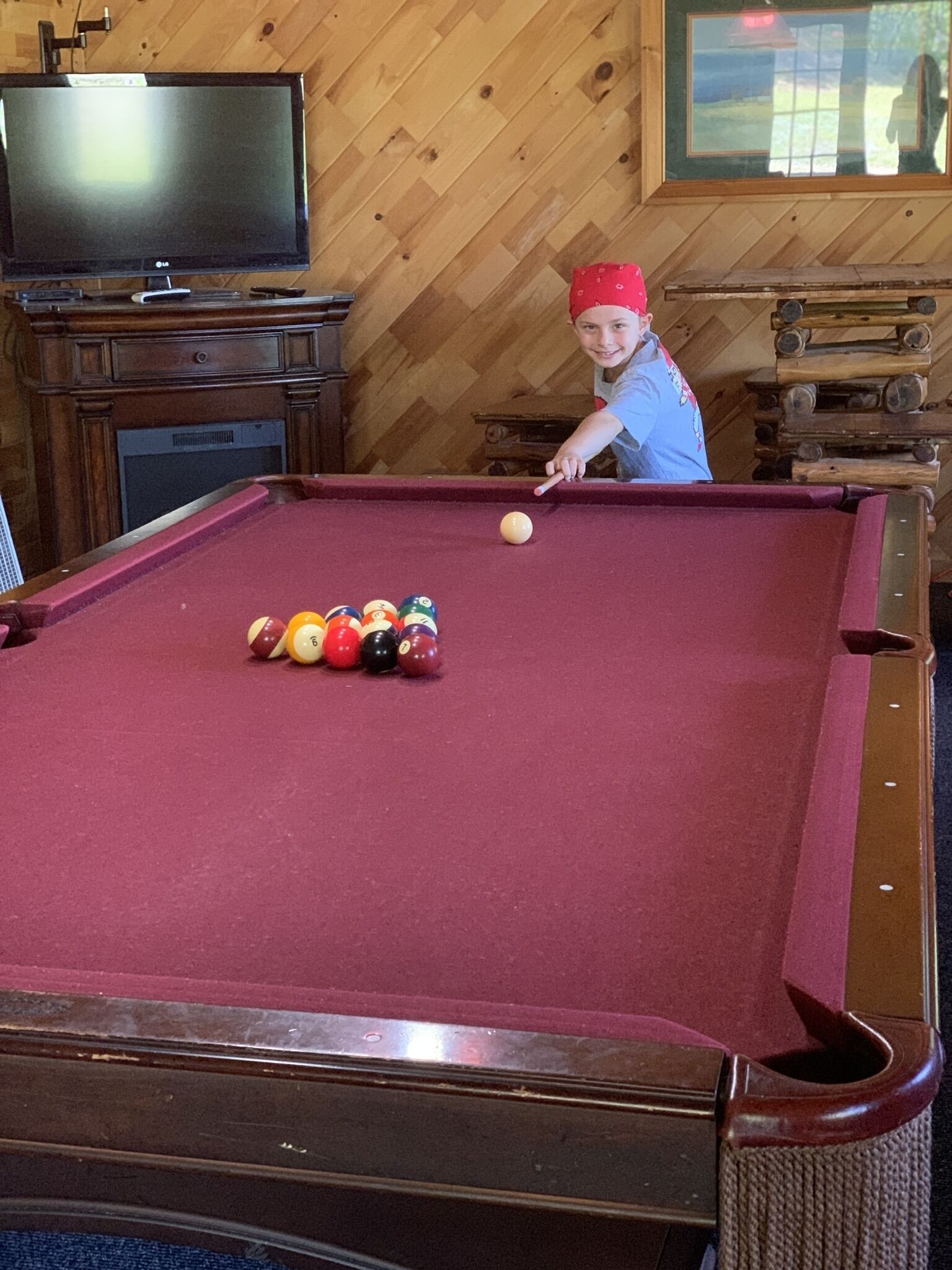 A pool table with balls, a television, and wooden paneling.