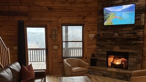 A cozy cabin interior with a stone fireplace, leather sofas, a wooden coffee table, and a TV mounted on the wall. - Deep Creek Overlook Cabin HGTV Log Cabin Living WiFi Pool Table Hot Tub King Bed (Bryson City)
