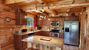 A wooden cabin-style kitchen with granite countertops, stainless steel appliances, and a central island with stools. - Deep Creek Overlook Cabin HGTV Log Cabin Living WiFi Pool Table Hot Tub King Bed (Bryson City)