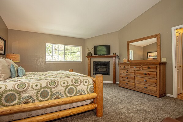 A bedroom with a bed, a fireplace, a television, and a dresser.